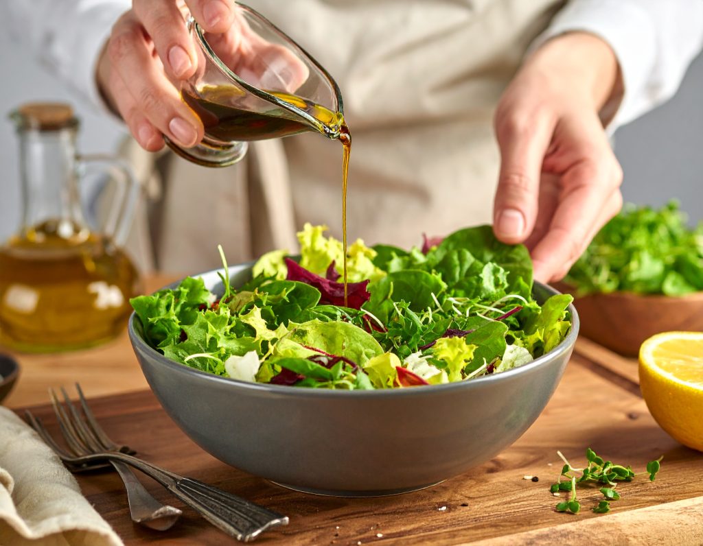 Blattsalat wird mit Dressing für die Kürbis-Quinoa-Bowl vermischt